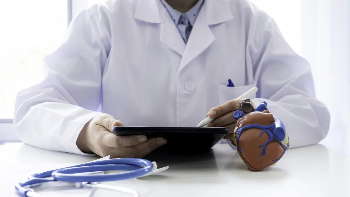 Docteur utilisant une tablette numérique avec un modèle de cœur et un stéthoscope sur le bureau
