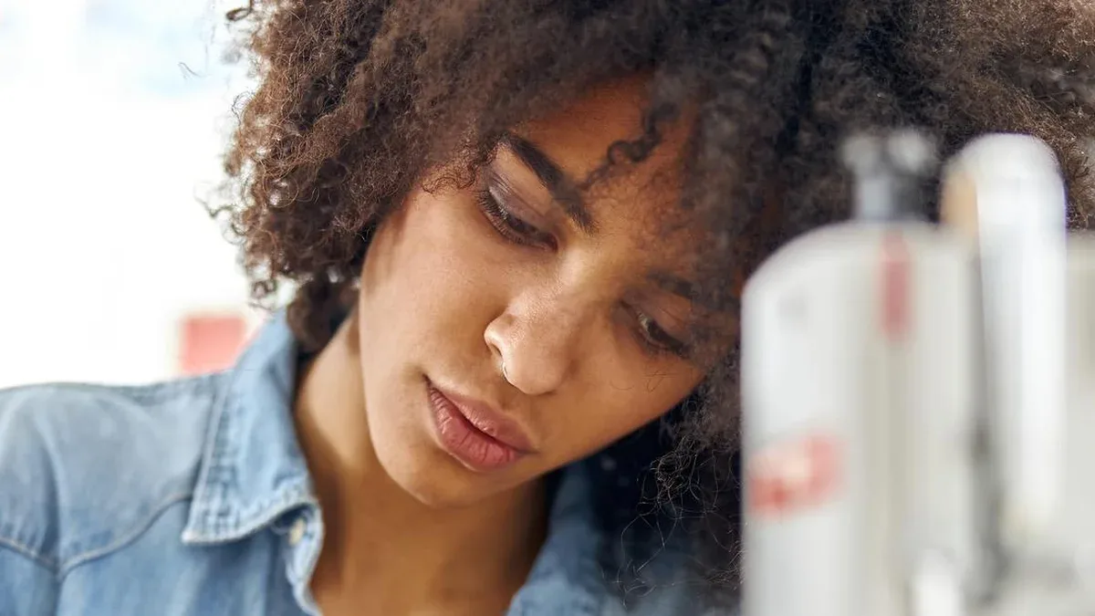 Une couturière afro-américaine concentrée dessine dans un carnet de croquis assis sur son lieu de travail avec une couture moderne