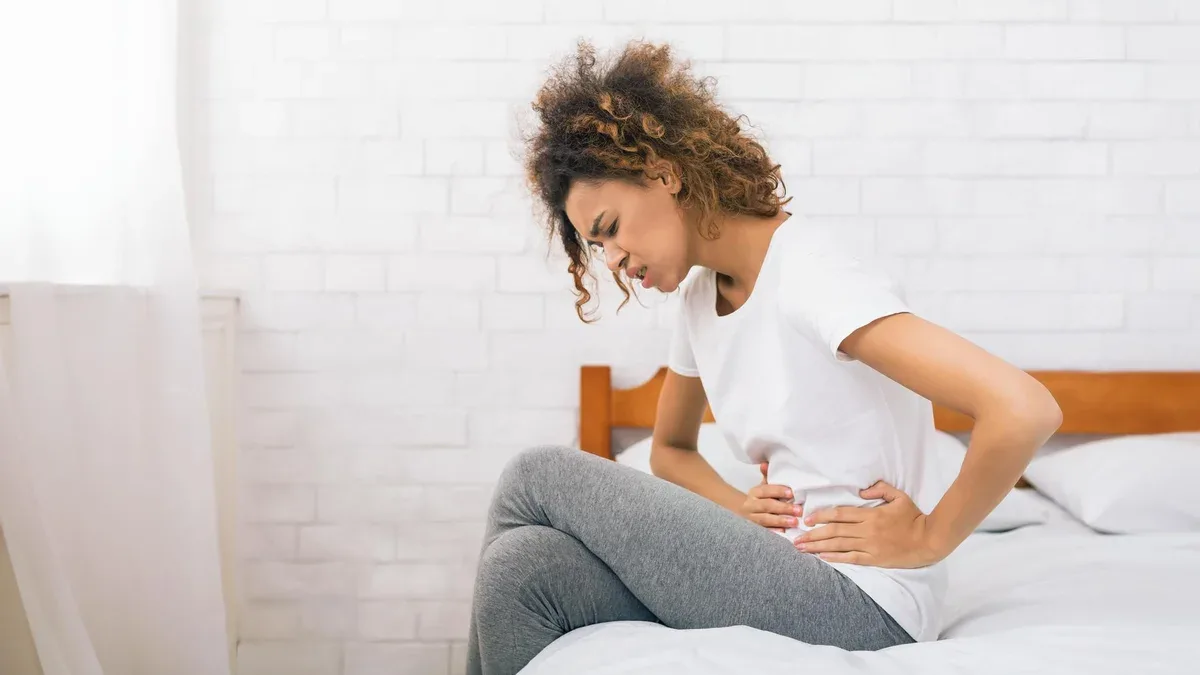 Une femme malheureuse souffrant de maux d'estomac assise sur le lit.