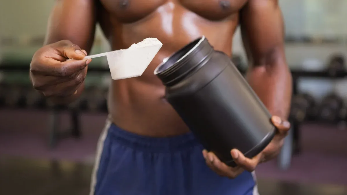 Body builder tenant un scoop de mélange de protéines dans un gymnase