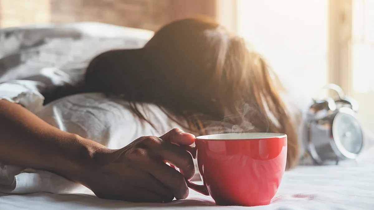 Belle femme asiatique assis dans le lit avec une tasse de café.