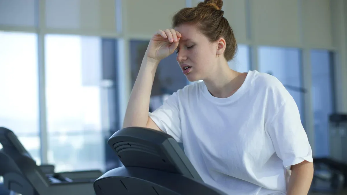 Une jeune femme fatiguée et épuisée s'entraîne à courir sur un tapis roulant dans une salle de sport en tenant sa tête avec