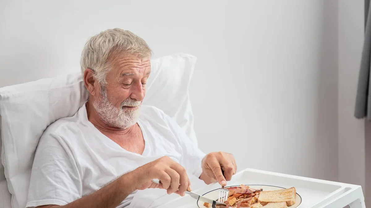 Homme senior âgé prenant son petit-déjeuner sur le lit dans la chambre à la maison de retraite