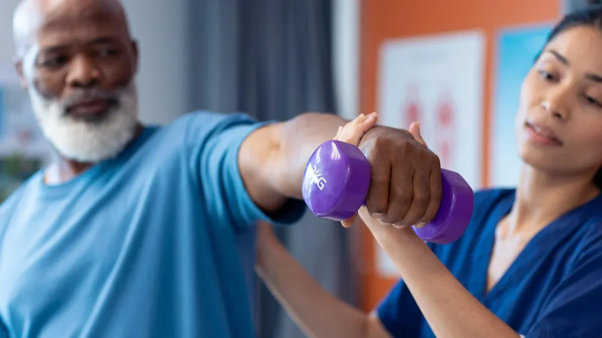 Physiothérapeute féminine diversifiée aidant les patients masculins âgés à faire de l'exercice avec des haltères, espace de copie.