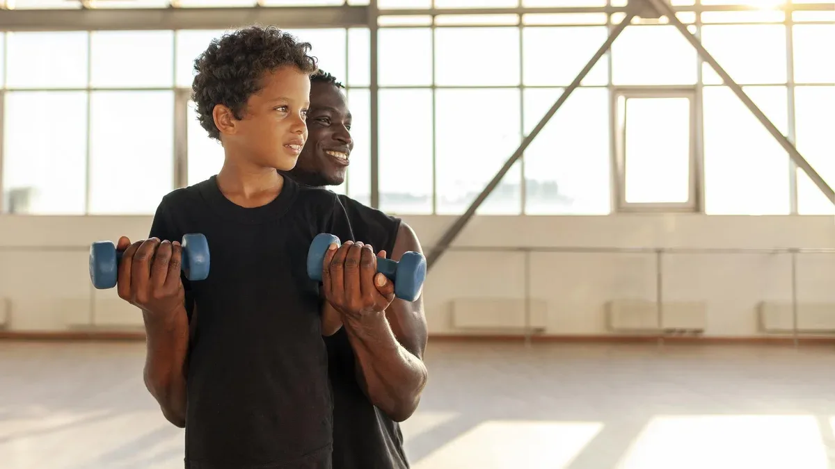 père et fils font du sport dans la salle de sport un homme afro-américain aide son fils à soulever des haltères