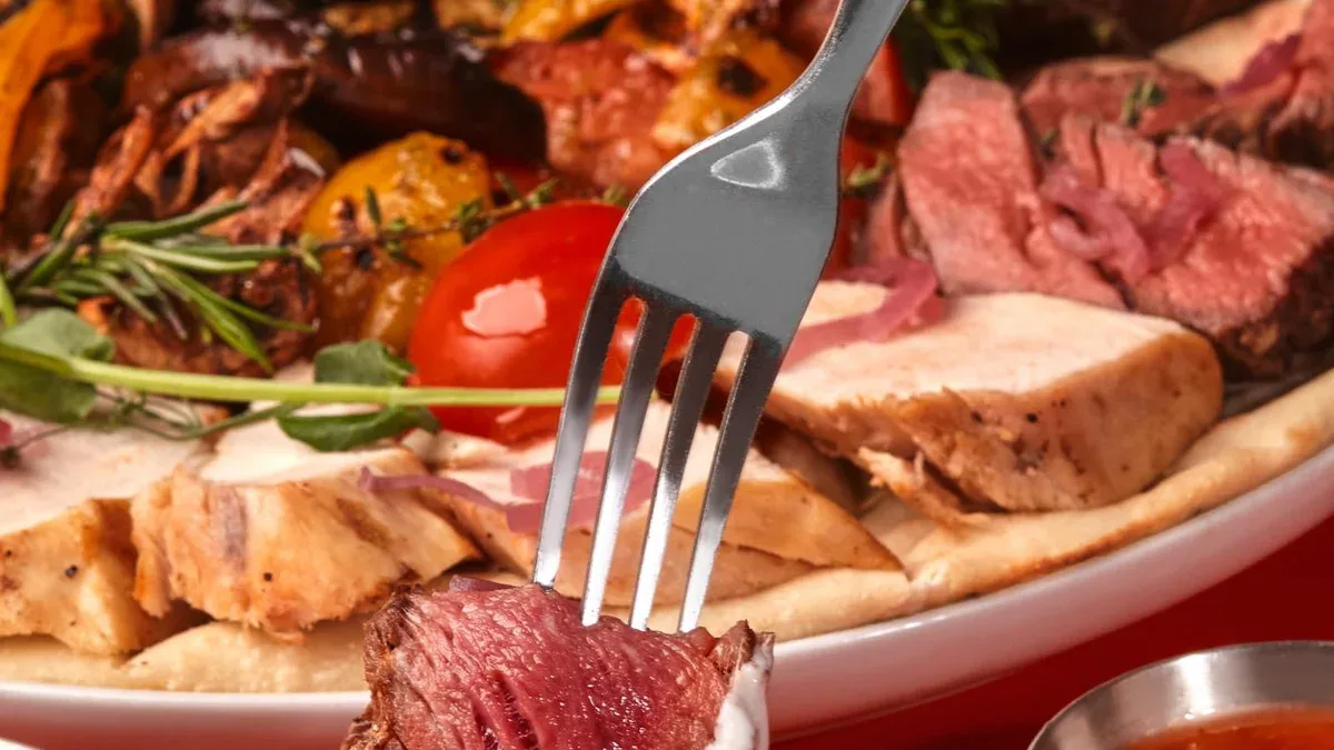 Une femme trempant du bœuf grillé dans une sauce blanche avec une variété de viande et de légumes grillés