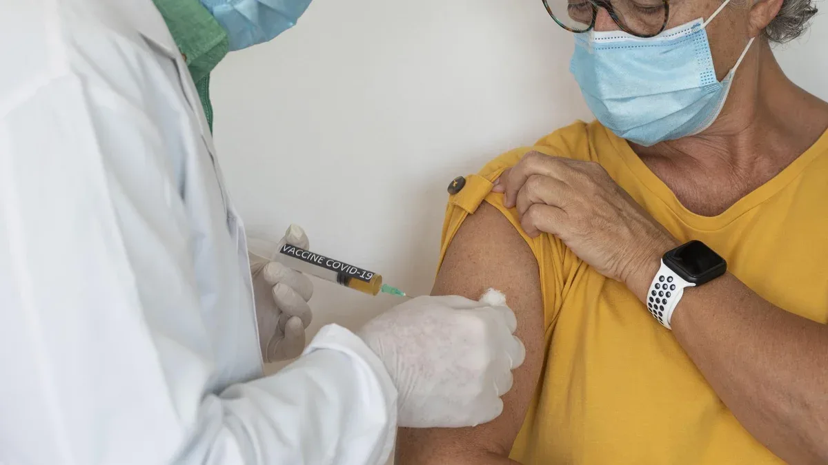 Coronavirus. Une seringue entre les mains d'un médecin injectant le vaccin contre le coronavirus covid-19 à une femme en chemise jaune